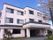 施設の建物は、白い外壁に瓦屋根のシンプルな外観となっている。玄関前に大きな屋根が設けられている。右側には桜の木がある。