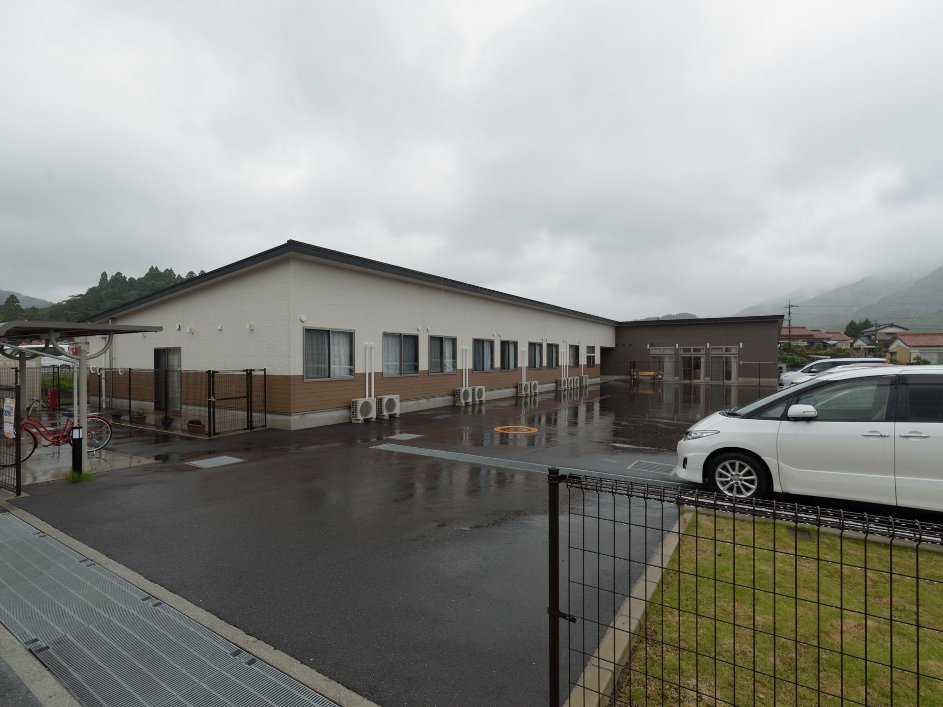 広い駐車場と、駐輪場も併設した平屋建てのホーム。周囲には住宅地などが並び、敷地の周りはフェンスで仕切られている。