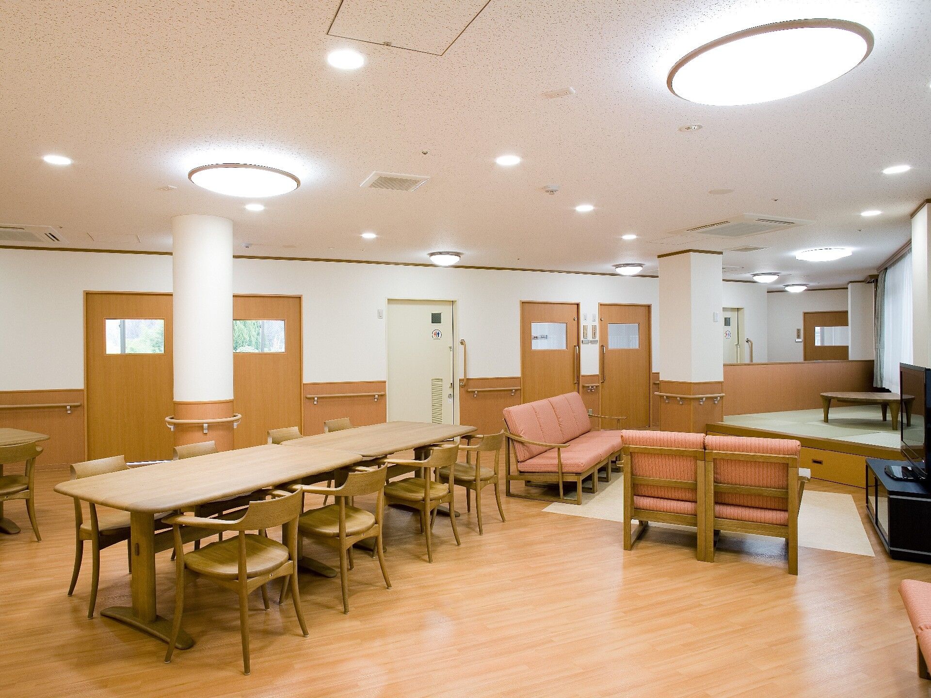 施設での食事前の配膳風景である。スタッフが細やかな配慮をしながら、テーブルに着かれている入居者様の前に配膳している。