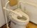 白い壁にフローリング床の洋式トイレである。便器を囲むように手すりが配置されている。壁には緊急時用の呼び出しボタンを完備している。