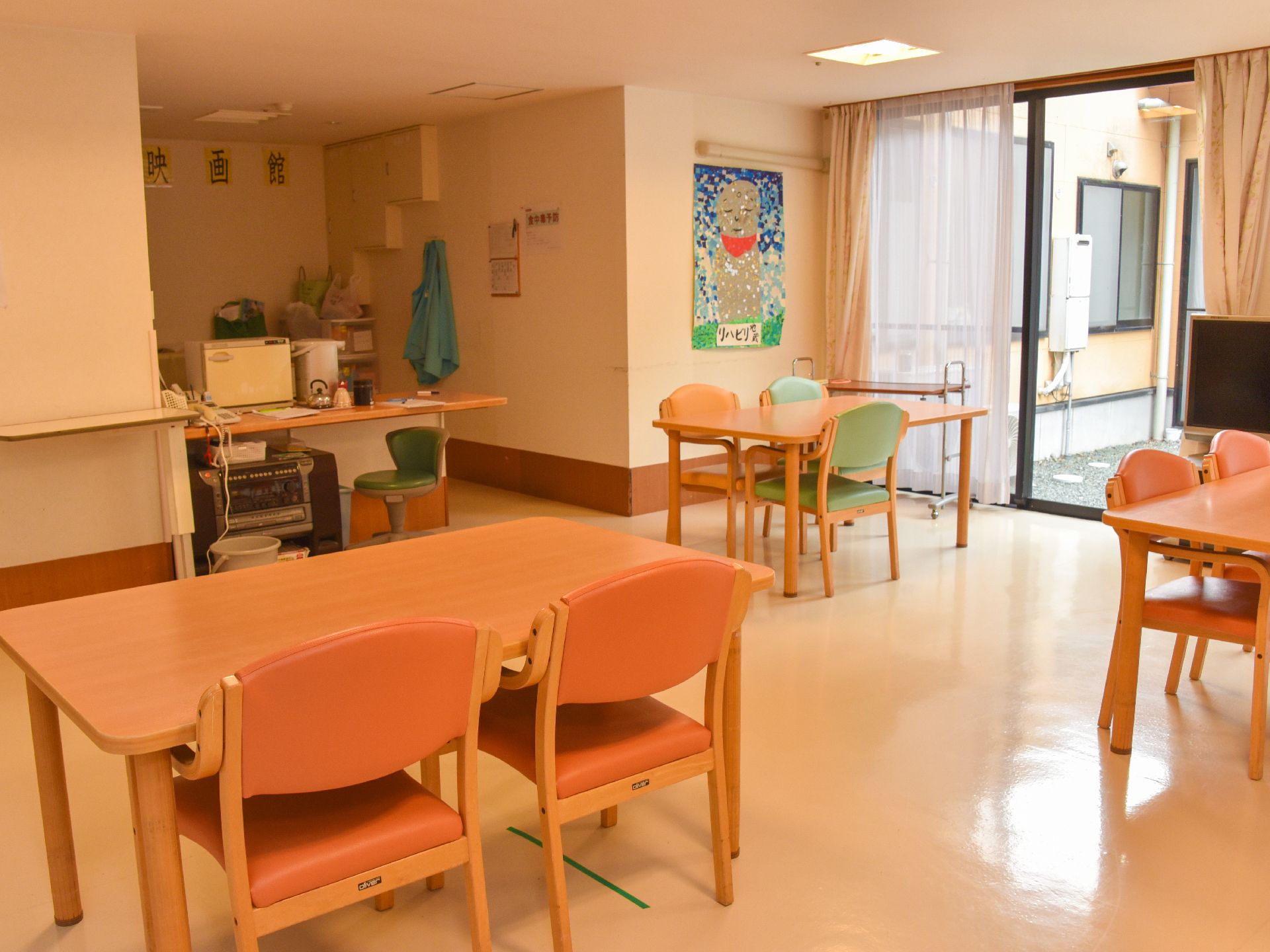 室内には余裕を持った間隔でテーブルセットが配置され、大きなガラス戸からは外を眺められる。壁にはお地蔵さんのちぎり絵が飾られている。