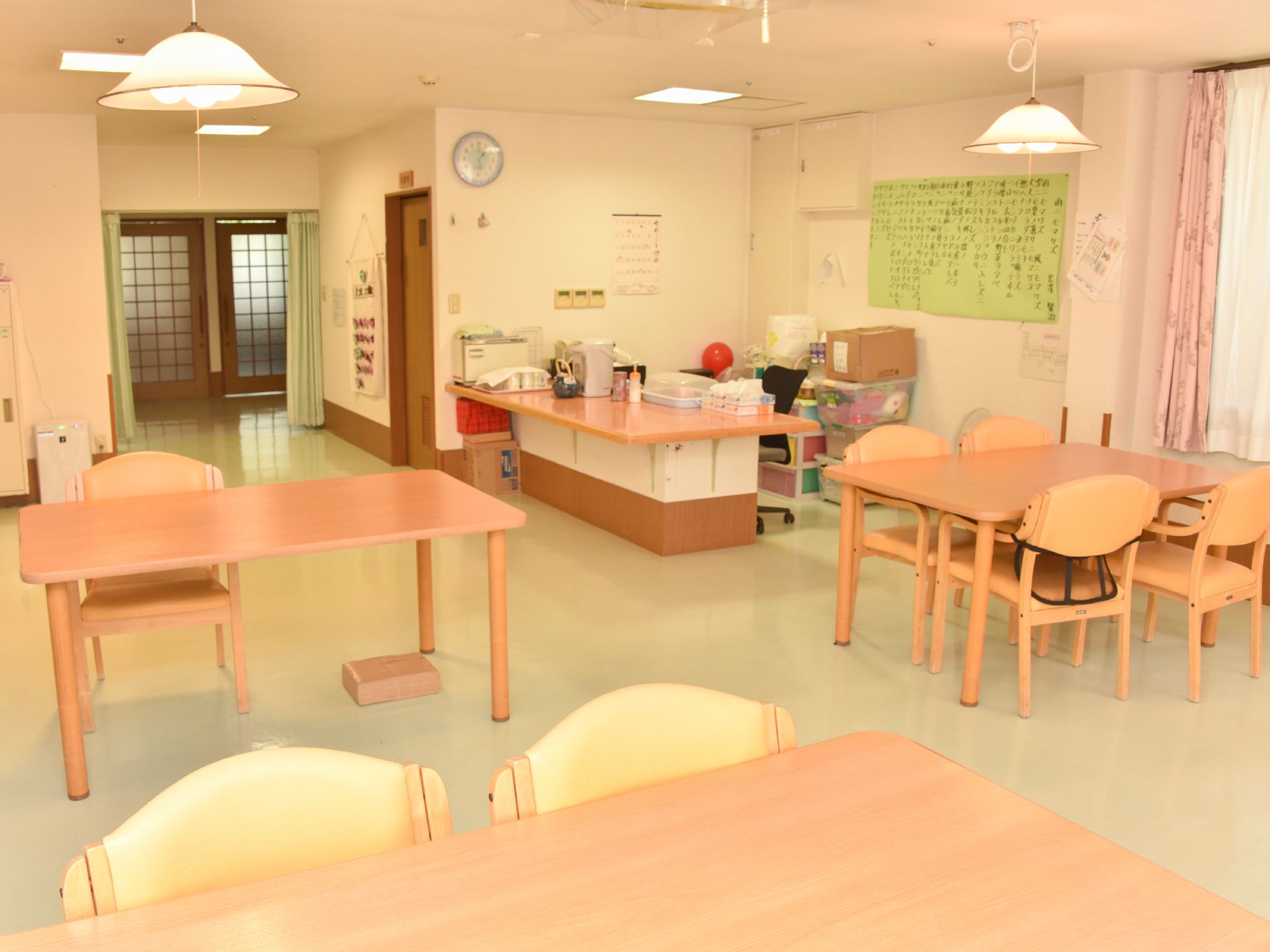 テーブルの並べられた食堂は多目的室としても利用されている。入り口のカウンターの周りには様々なものが置かれている。