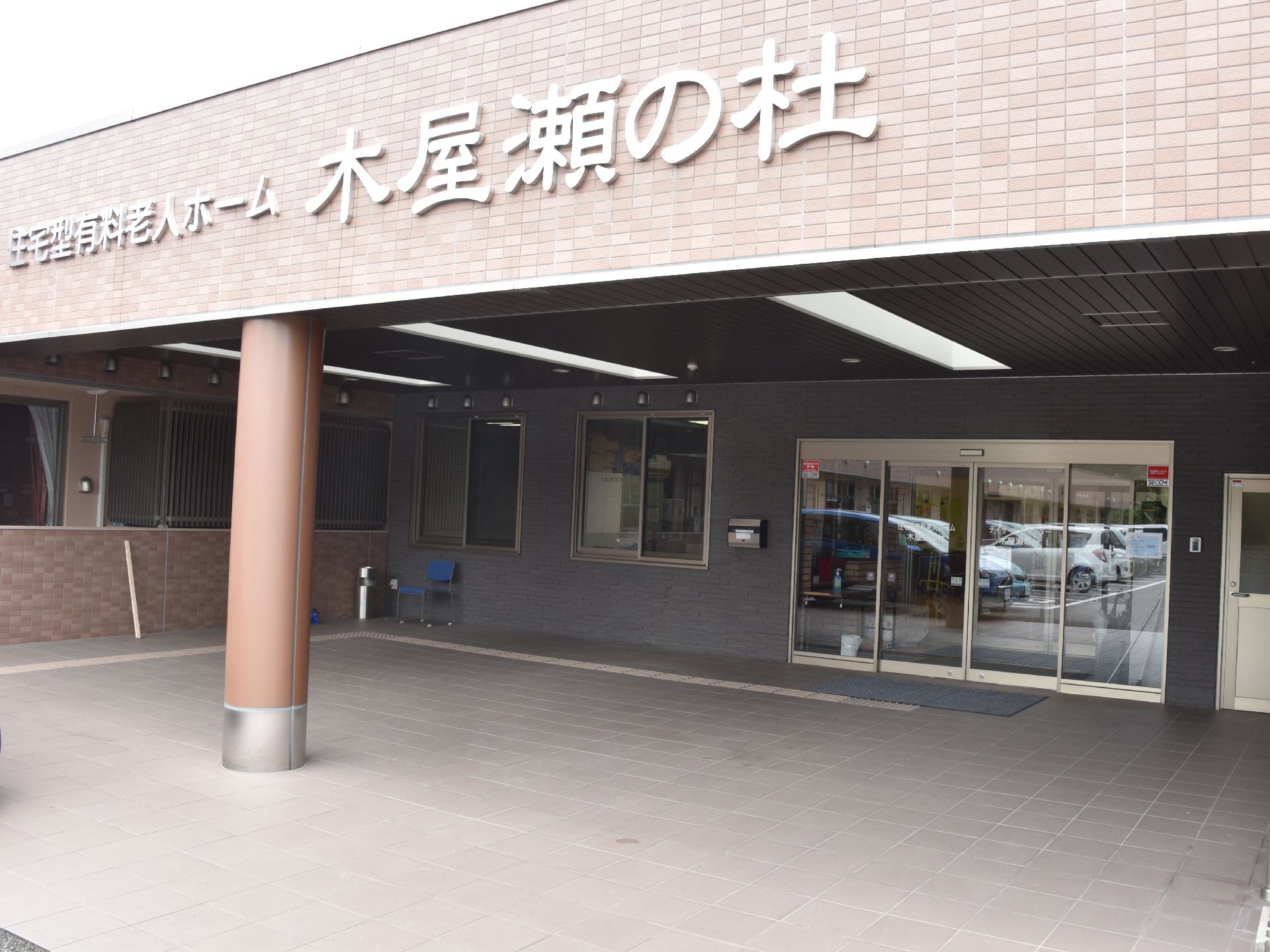 上部に大きく施設名の書かれた施設の入り口。ひさしのついた部分が広く設けられている。ガラス張りの自動ドアと横にももう一つドアが並んでいる。
