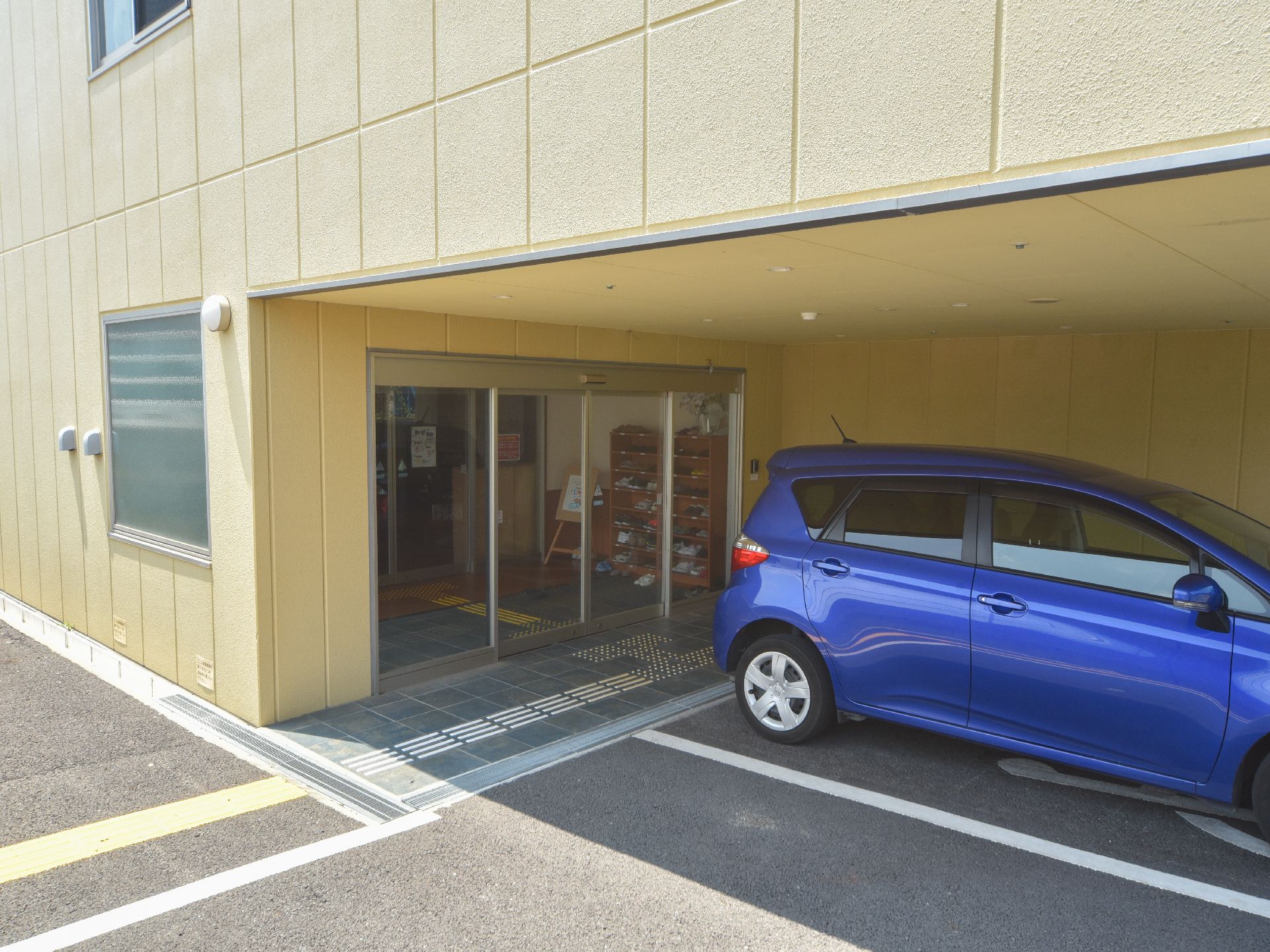 建物1階の一角を凹部とし、出入り口に充てている。門前は車寄せになっており、青い自動車が停められている。
