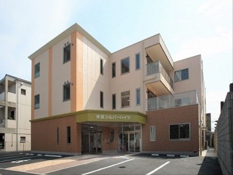 ３階建ての建物が見える。玄関にはひさしがあり、正面には施設名が掲示されている。バルコニーが２階と３階に設けられている。