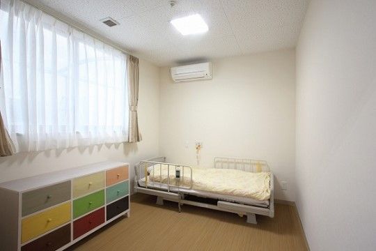 居室の向かって正面の壁にエアコンが設置されている。大きな窓にはカーテンが取り付けられており、レースカーテンが閉められている。