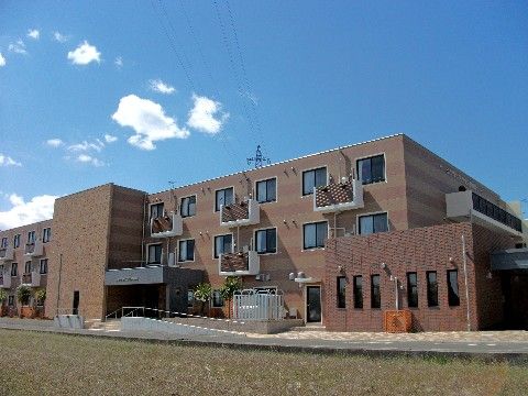 玄関へのスロープが設置された、３階建て、ライトブラウンの施設の外観
