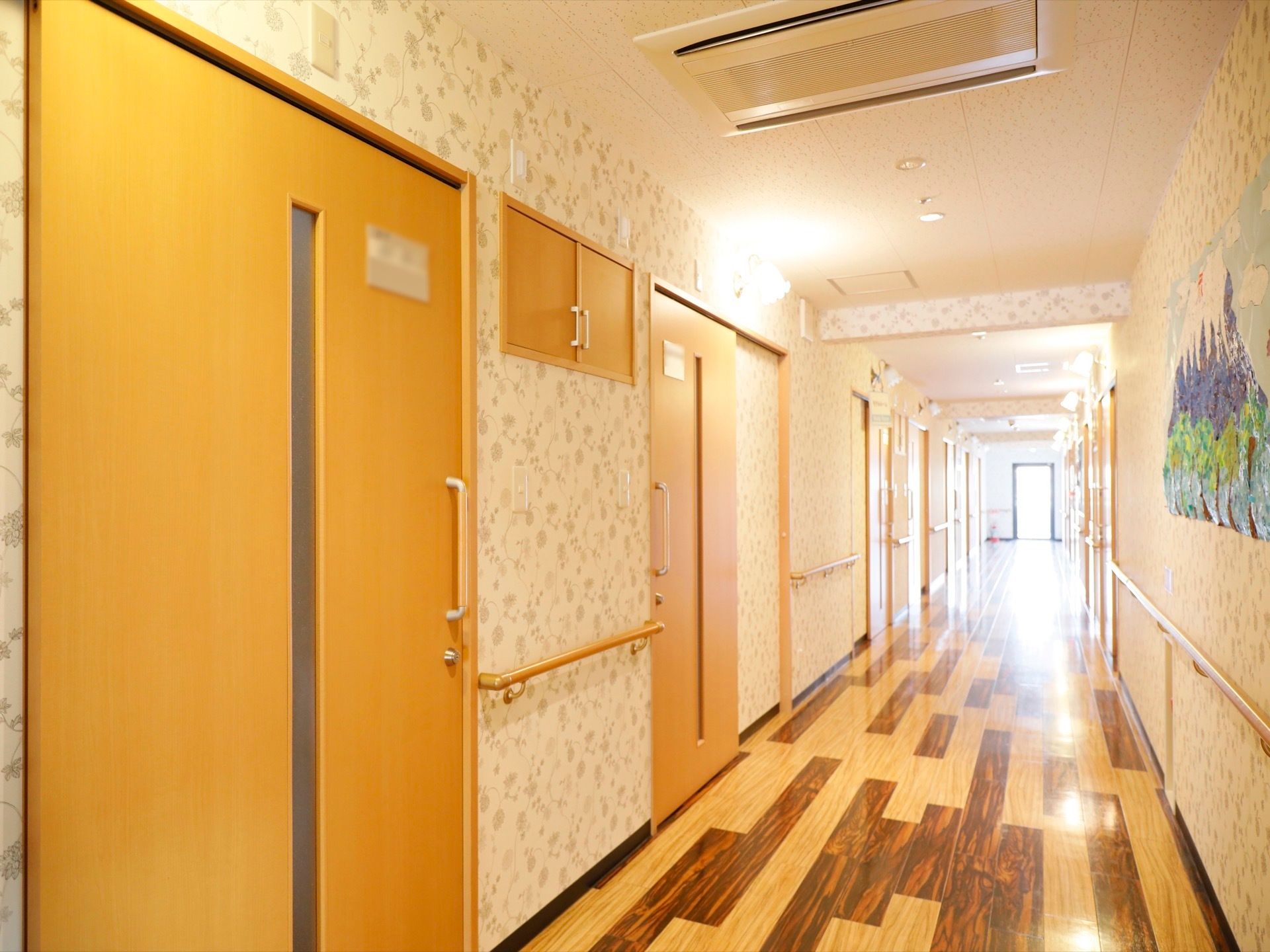木目調の床が優しい雰囲気を漂わせている。広い直線の通路は明るく、壁に山を描いたちぎり絵が掲示されている。