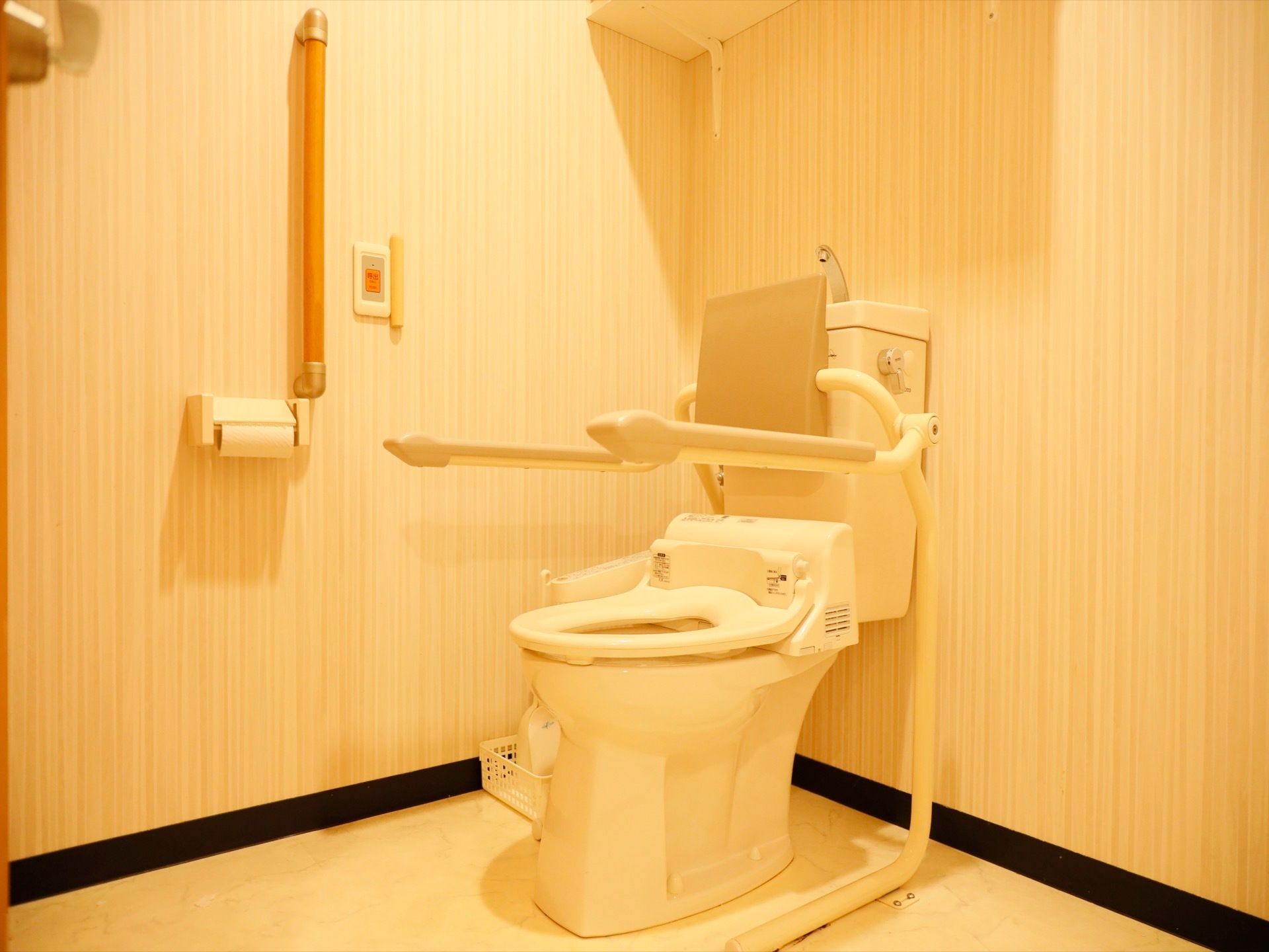 トイレの様子。温水洗浄便座の両側に可動式の手すりがついている。壁に手すりやナースコールが設置されている。