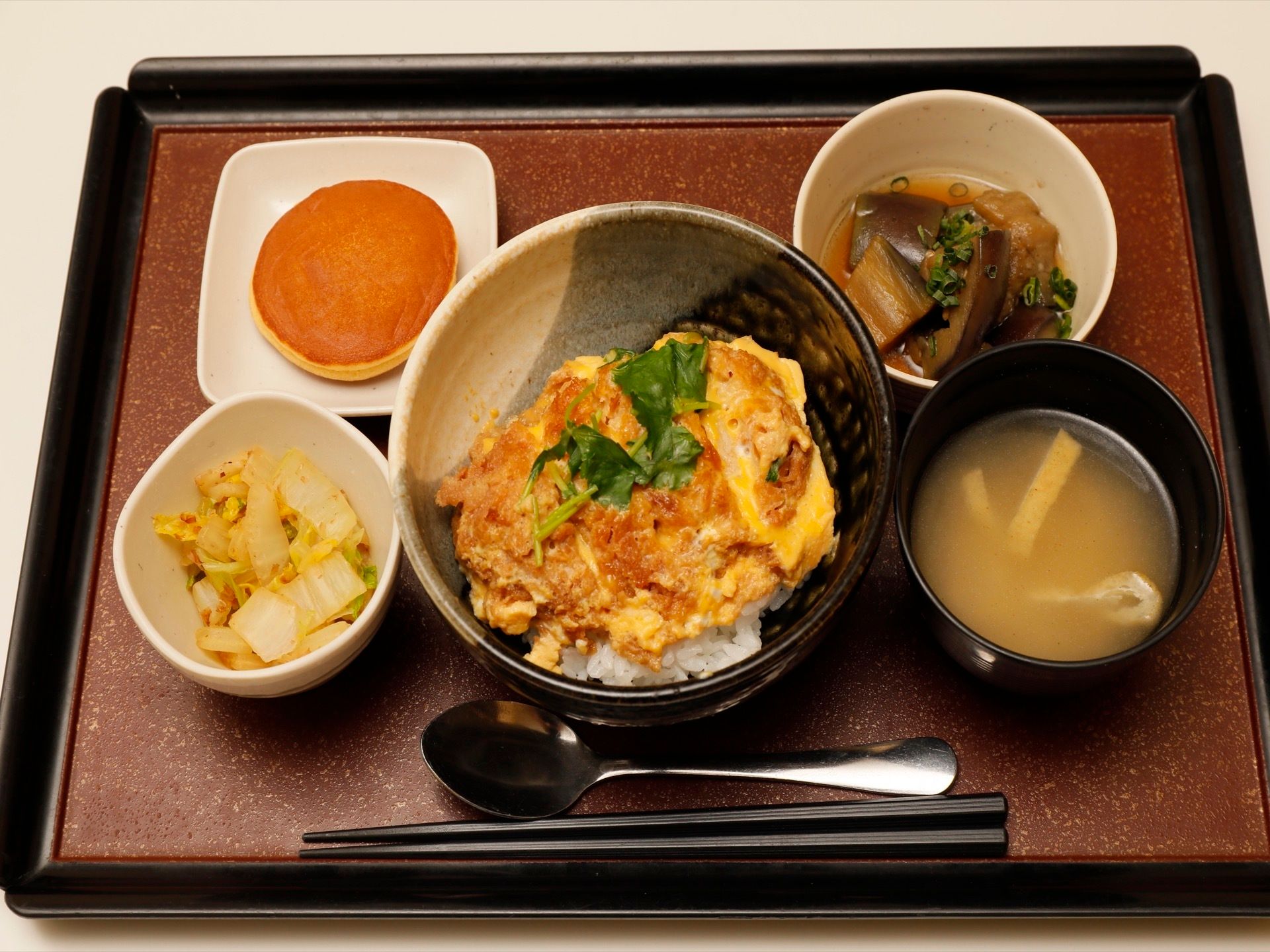 食事の様子。お膳にカツ丼となすの煮浸し、白菜の和え物、味噌汁、どら焼きが並べられ、スプーンとフォークが添えられている。