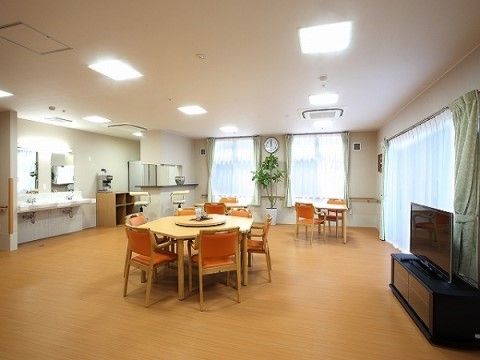 淡い色でまとめられたホール。中央に六角形のテーブルセットが置かれている。手前右にテレビ、左壁に洗面所が設けられている。