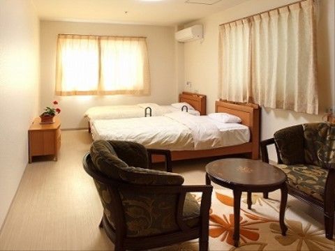 葉っぱの模様の入ったカーペット敷きの部屋である。ミニテーブルとソファチェアのセットがあり、奥にはベッドとサイドボードが置かれている。