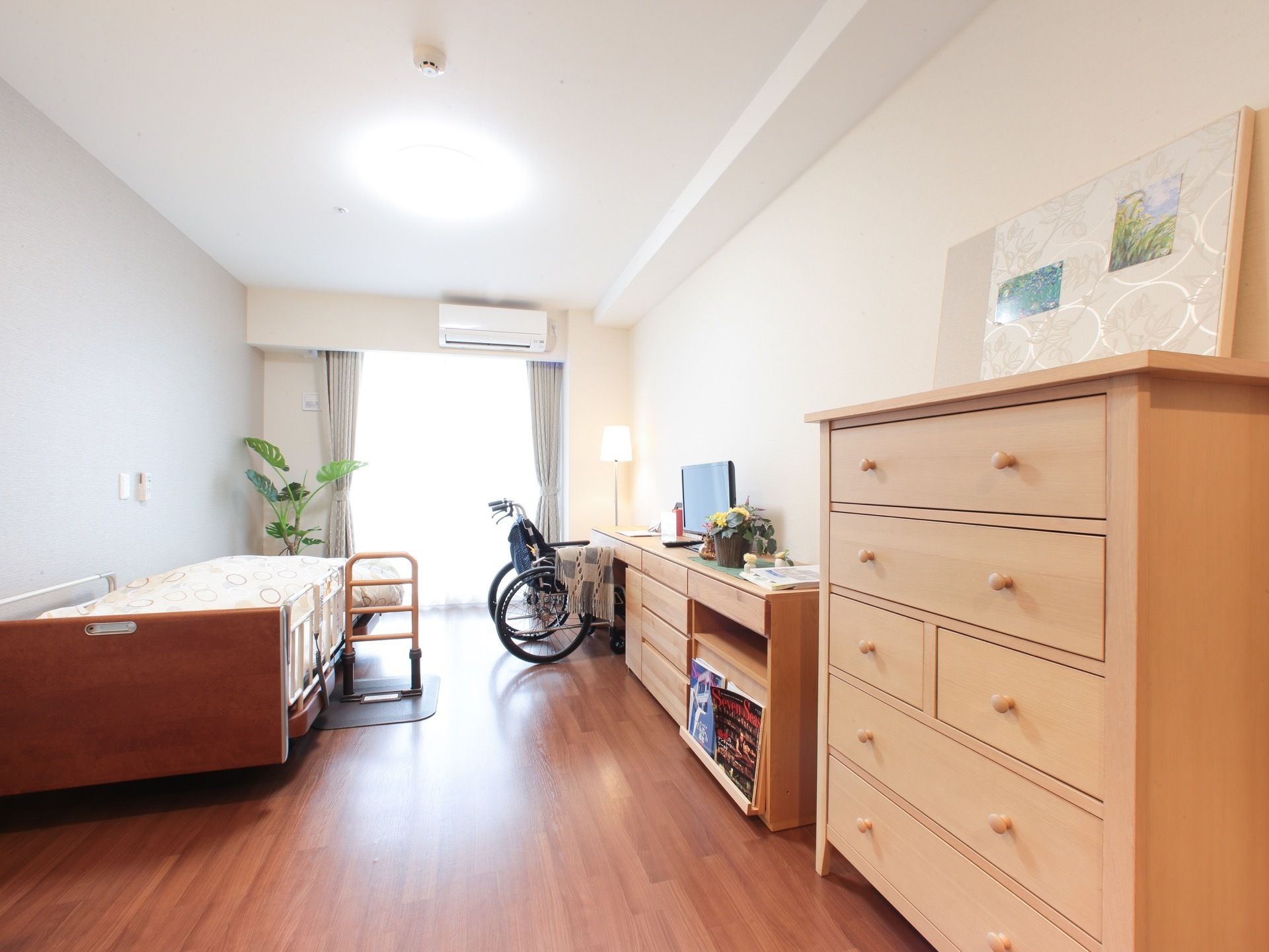 ベージュ色の収納家具とベッド、車椅子がある明るい雰囲気の部屋