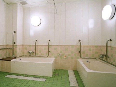 明るい浴室の左側にある浴槽には、壁と一体化した台が設けられている。手すりもあり、入居者様は安全に座ることができる。