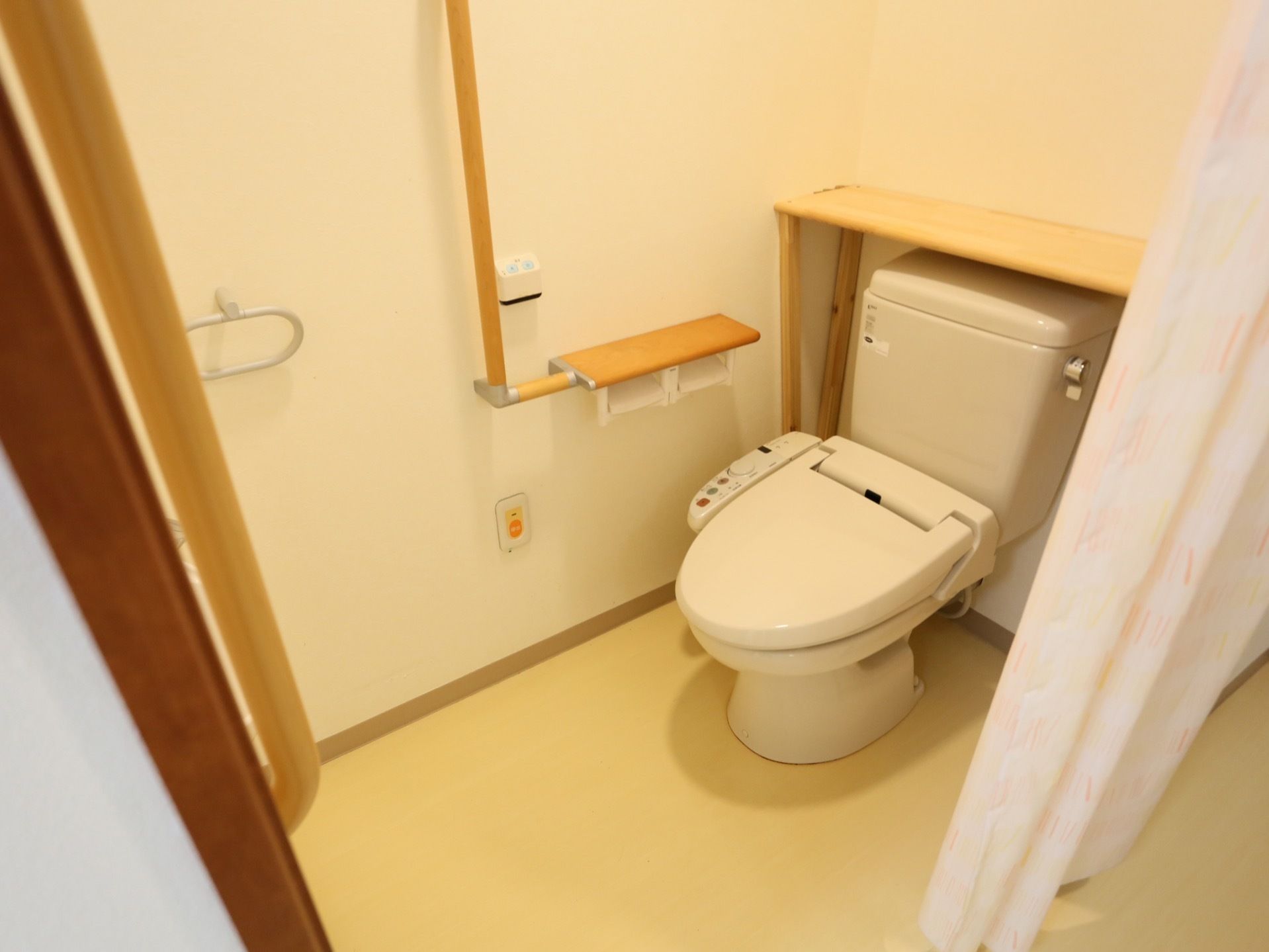 居室のトイレには、手すりや温水洗浄便座、呼び出しボタンが完備されている。カーテンが扉に採用されている。