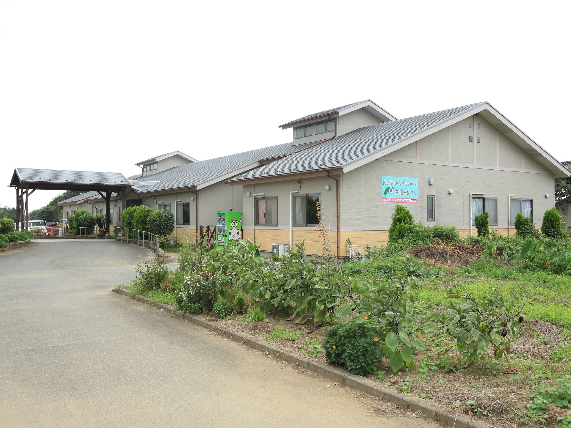 施設の建物は平屋建てで、一部に高くなっている箇所がある。右側の壁には施設名が表示されている。周りには植物が植えられている。