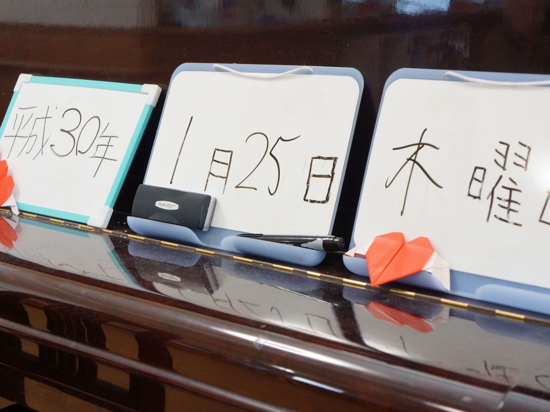 施設では壁にホワイトボードを三つ並べ、日付や曜日を毎日書き込んでいる。折り紙で作った飾りで彩りを添えている。