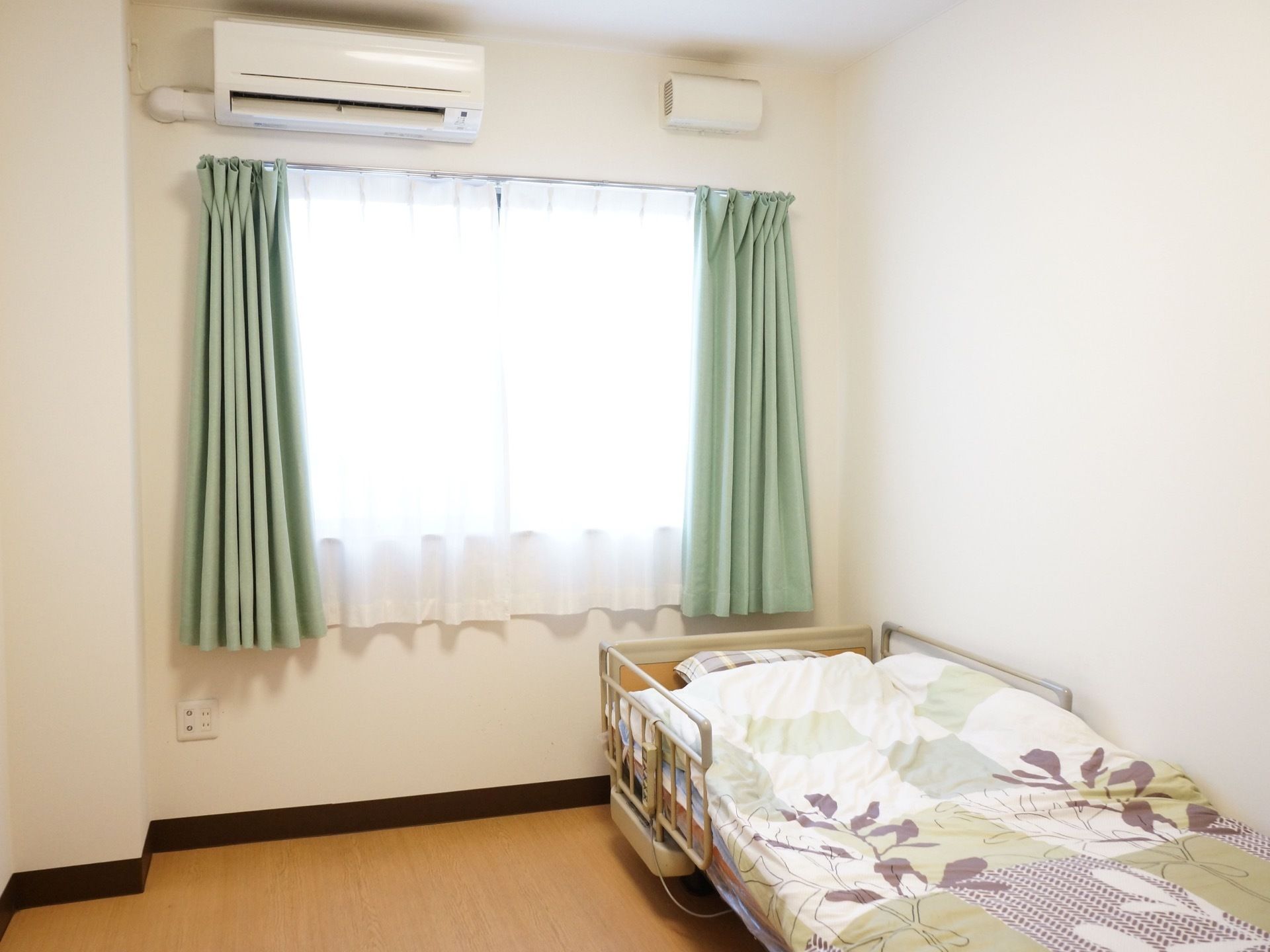 居室の床は全面フラットなフローリングである。電動ベッドには安全性に配慮して落下防止用のフェンスを設置している。
