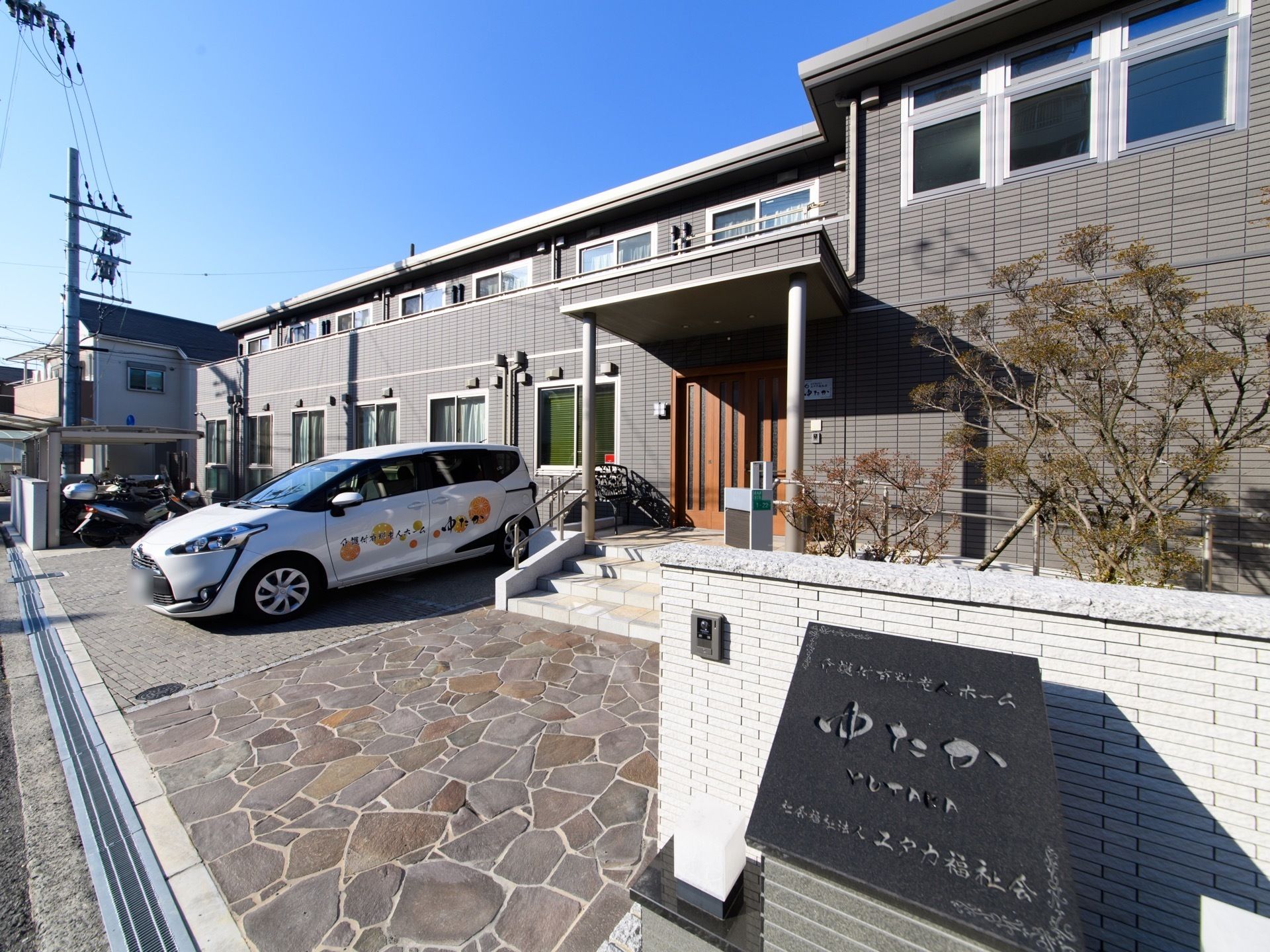 住宅地にあるこじんまりとした２階建ての施設。入り口の階段に手すりがあり、スロープも付いている。２階はベランダの塀が高いので安心。