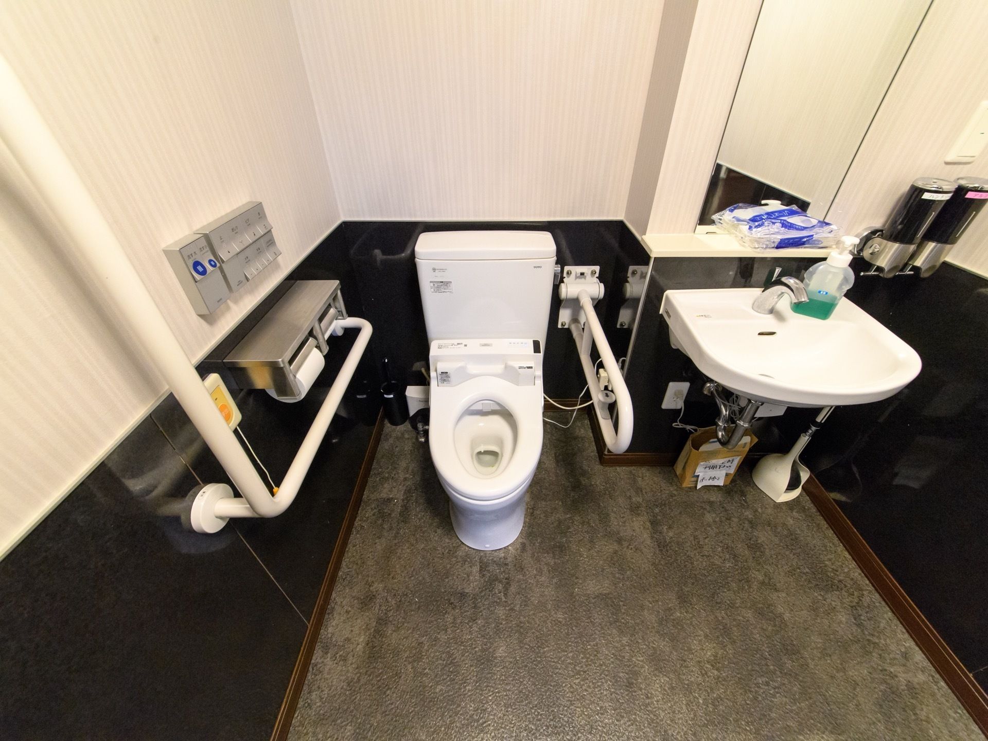 トイレは白と黒のシックな壁。手すりが付いて車椅子をご利用の方や杖の方でも安心。洗面台も大きく、シャンプー、リンスも付いている。