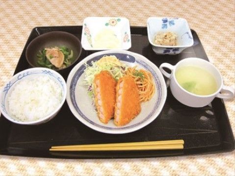 黒いお盆の上に料理が盛られた小皿が置いてある。コロッケをメインにしつつ、サラダや漬物によりバランスの良い食事である。