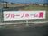 施設内のフェンスに横長の看板が付けてある。白地にワインレッドの色で施設名が書かれてある。施設名をイメージするような色である。