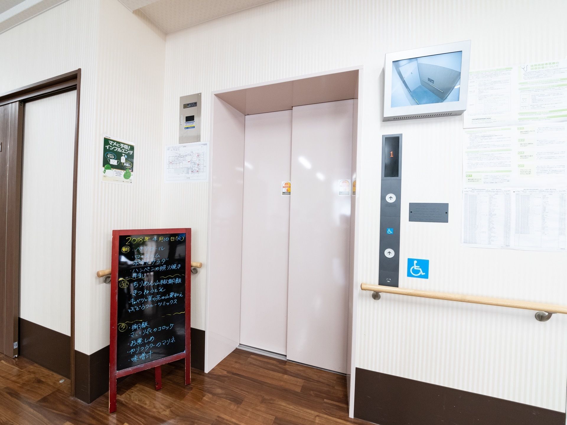エレベーターの前は広く明るくなっている。内部の様子がわかるモニターがつけられている。扉の前には食事のメニューボードがある。