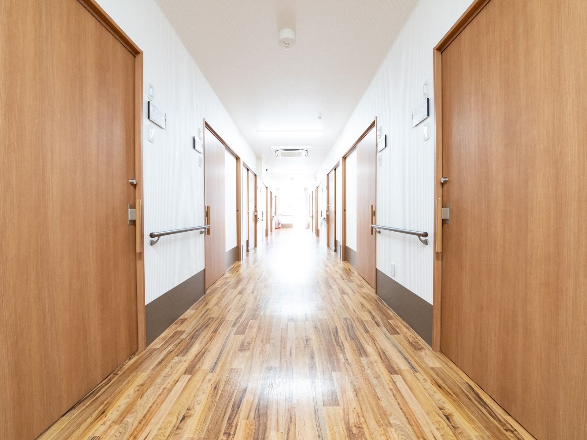 明るくて広々とした廊下。余計な物が置いていない。壁には手すりが設置されている。床はフローリングで段差がない。