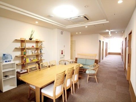 一直線上に伸びた廊下は幅が広く、照明や日の光により明るく保たれている。談話スペースには、数冊の書籍や観葉植物が飾られたオシャレな棚がある。