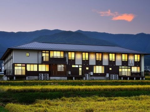 「サービス付き高齢者住宅　ゆうちゃん家」の外観全景夕景（東面）。自然の緑と、広い空の夕景が美しい。
