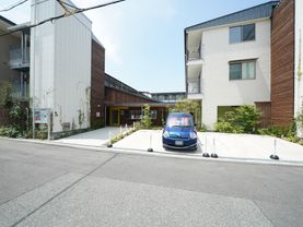 白とウッド調を基調としたモダンな雰囲気の外観である。建物の前には駐車スペースがあり、車が１台止まっている。