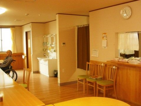 左手にテーブルがあり、車椅子をご利用の方の姿が見える。右手前には食堂のようなカウンターがあり、その下に椅子が３脚並んでいる。