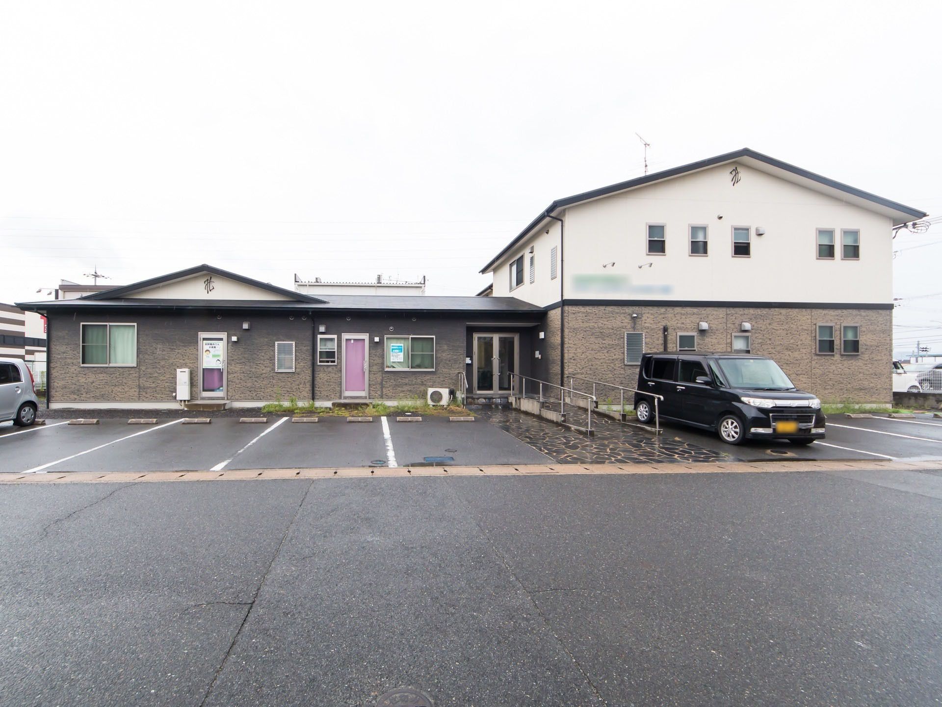ダークブラウン色とベージュ色が基調の落ち着いた雰囲気の建物である。玄関までの通路には、階段とスロープが設置されている。