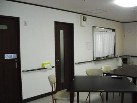 テーブルが２台と椅子が３脚ある。壁伝いに手すりがあり移動も安全に行える。ドアが二か所あり、左側はお風呂の入り口である。