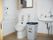 窓の前には洋式便器が設置されている。壁側にはトイレ操作ボタン、ペーパーフォルダー、手すりがある。便器横には大きなゴミが置かれている。