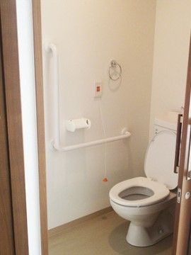 ドアが開いており、中に洋式トイレがある。トイレのフタは開いていて、便座は下りている。壁には手すりが付けられている。