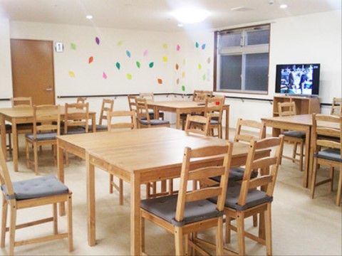 白い壁に、さまざまな色の紙が貼り付けられている部屋。木製の収納箱の上にはテレビがあり、何かの番組が映っている。