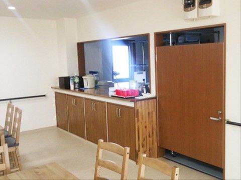 大きな茶色の扉で仕切られた部屋。手前の部屋には椅子やテーブルがある。奥の部屋には窓があり、強烈な光が差し込んでいる。