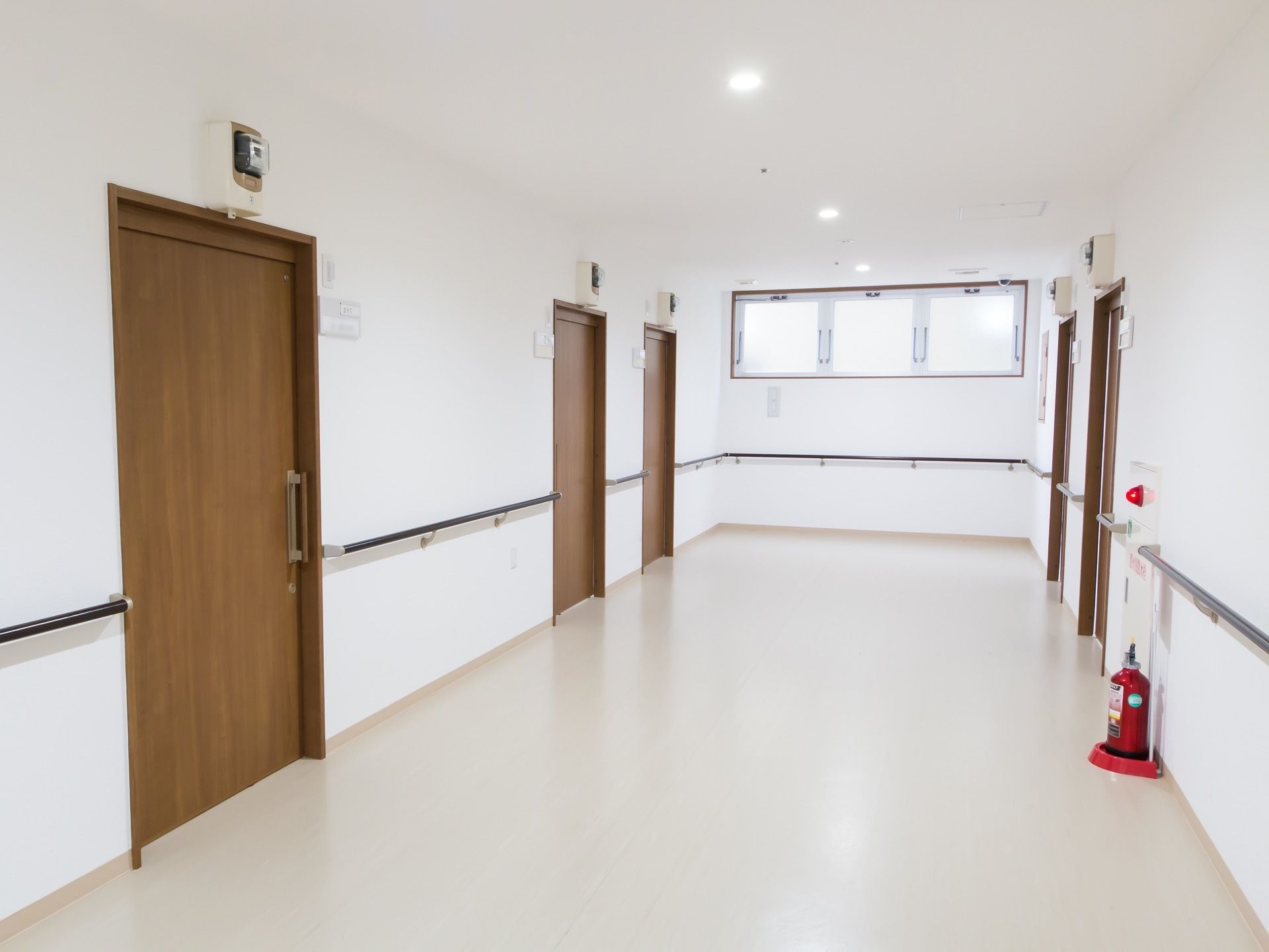 広い通路の両脇に居室ドアが並んでいる。突き当たりには高窓がある。壁には手すりが設置され、消火設備が整えられている。