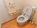 白い壁の清潔感のあるトイレになっている。手すりがＬ字型に設置してあり、安全に利用することができる。床はフローリングになっている。