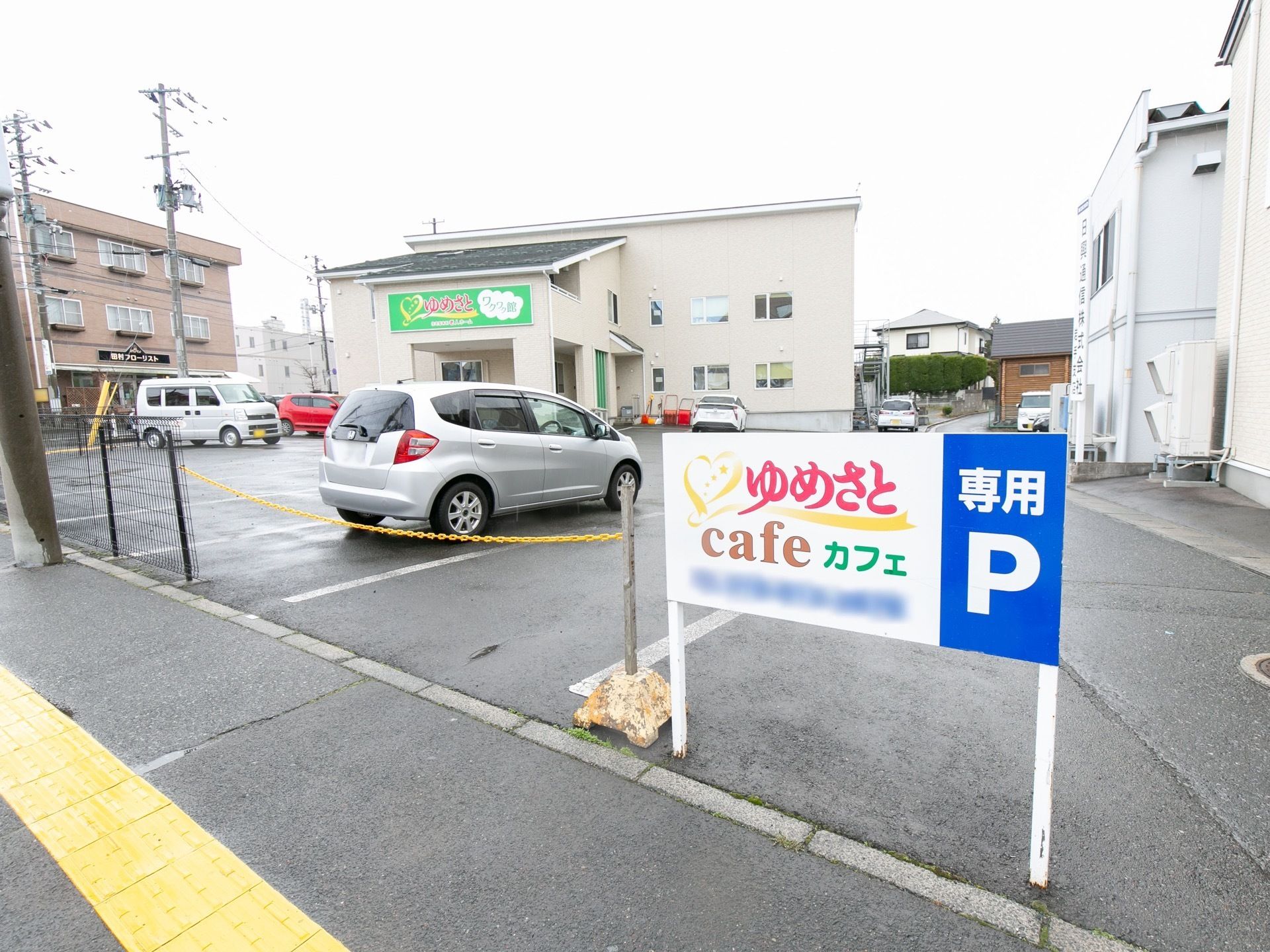 外壁は白で統一されており、施設名が記された看板が設置されている。駐車場には車が何台か停められている。