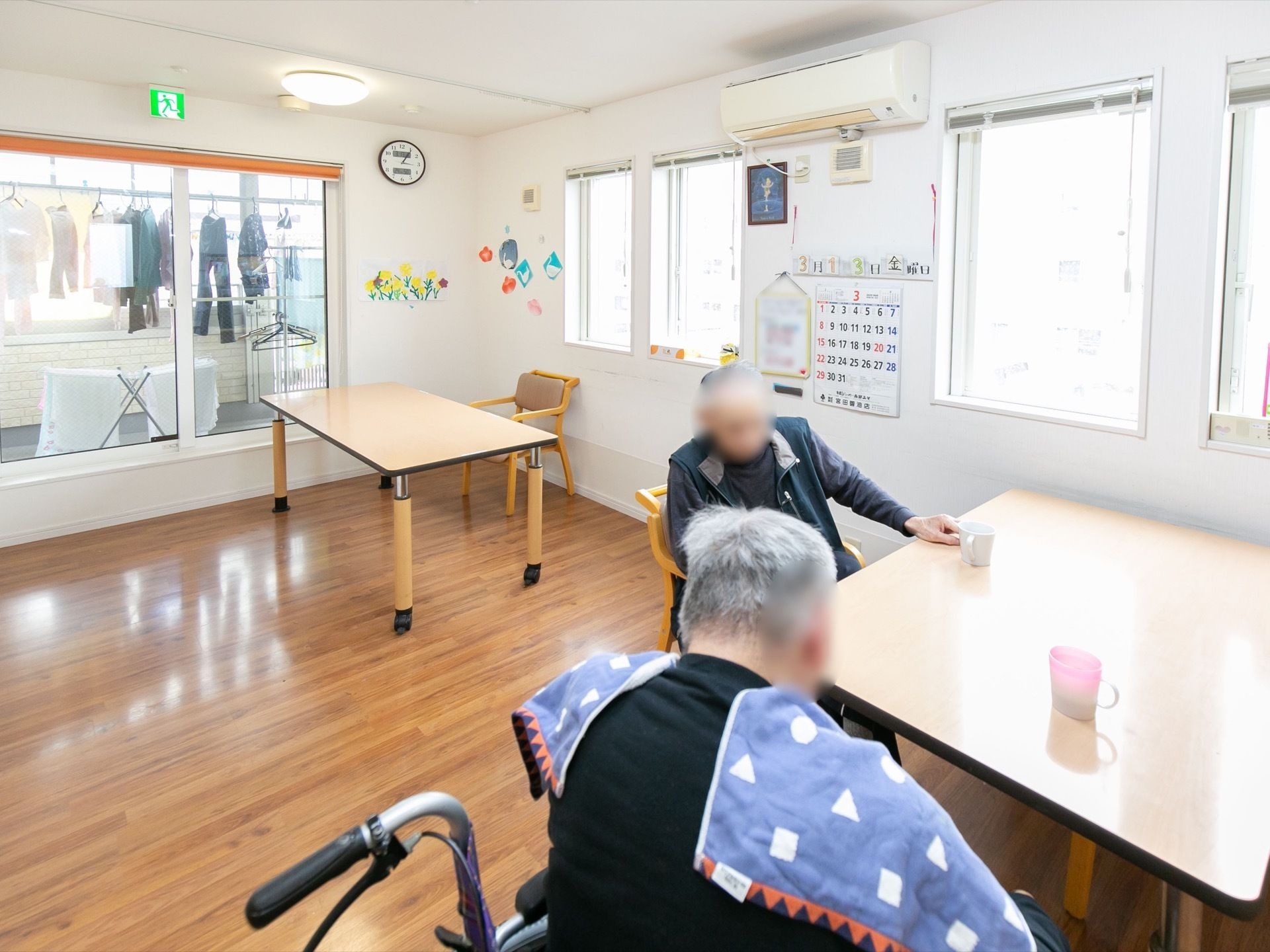 共有スペースでは、男性の入居者が自由に過ごしている。外には洗濯物が干されており、室内にエアコンが設置されている。