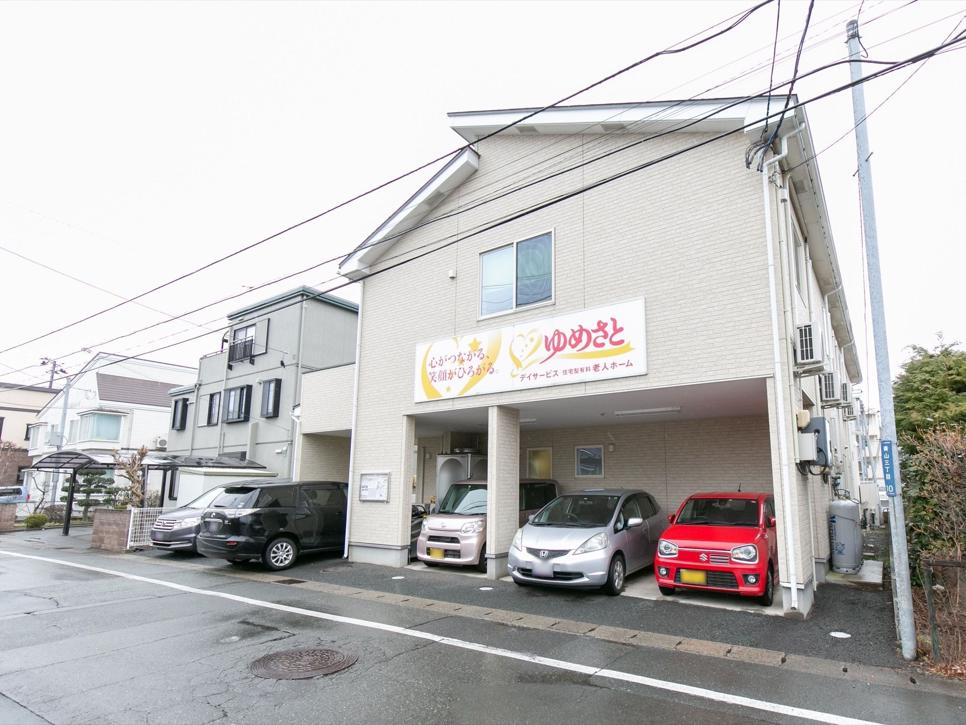 一軒家風の建物である。外壁には施設名が記された看板が設置されており、道路から目立ちやすい。駐車場には車が数台停まっている。