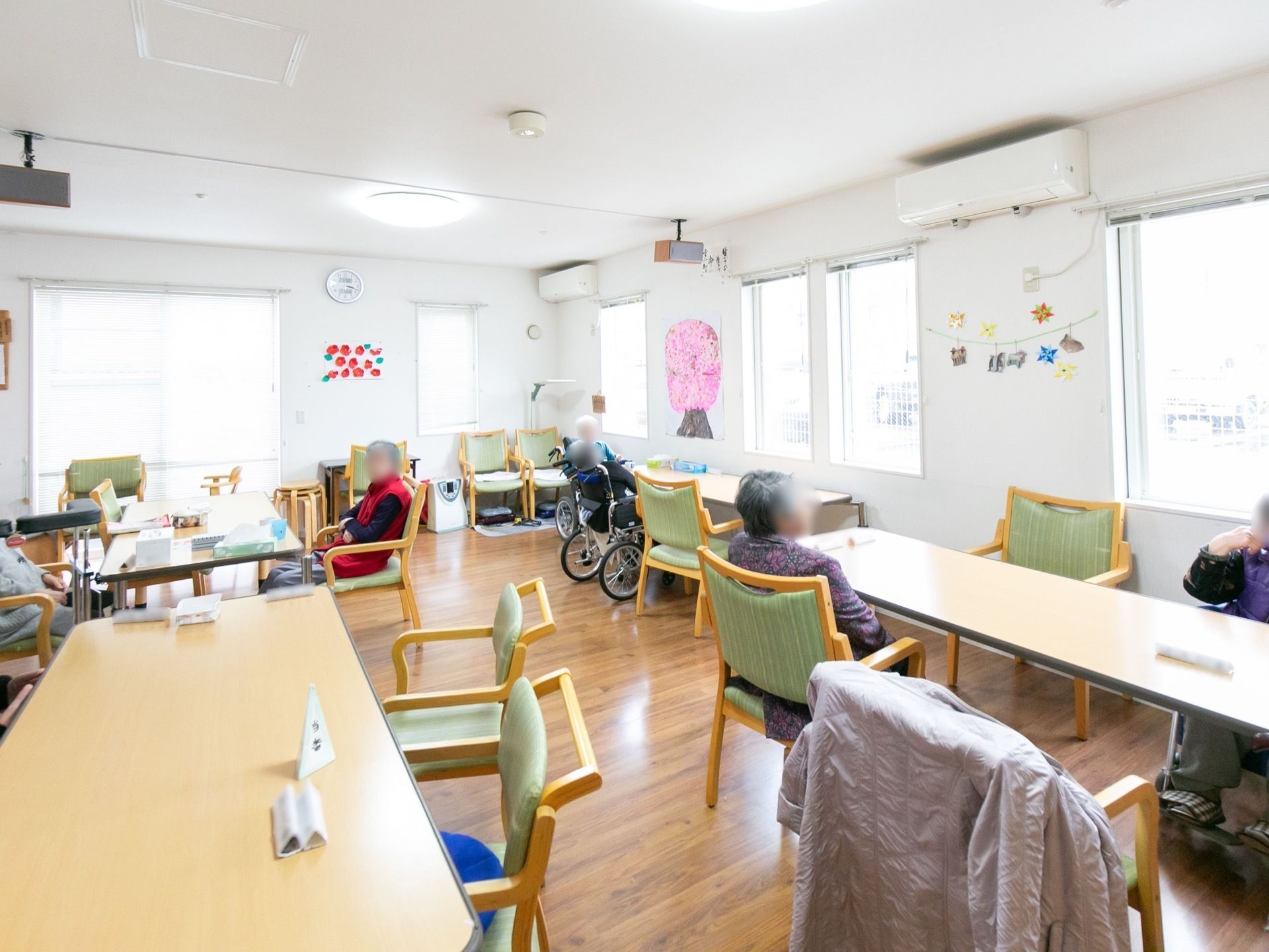 白い壁と木目調の床が落ち着いた雰囲気を醸し出すリビングルームで寛ぐ入居者
