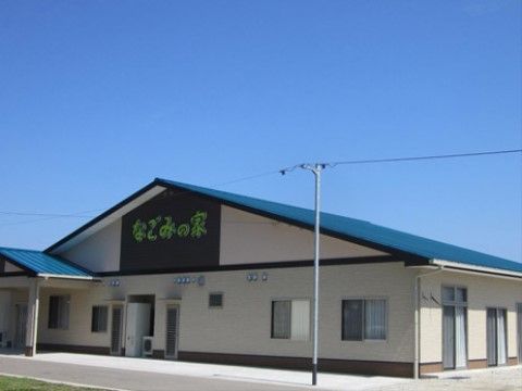 澄み渡る青空の下に、青い屋根の平屋建ての建物がある。壁に黄緑色の文字で施設の名称が表示されている。建物の前に細い電柱が立てられている。