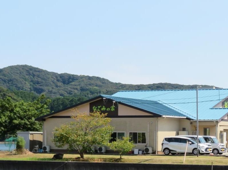 雲一つない快晴の空の下、ベージュ色の壁に青色の屋根の平屋建ての建物がある。壁に黄緑色の文字で施設の名称が表示されている。