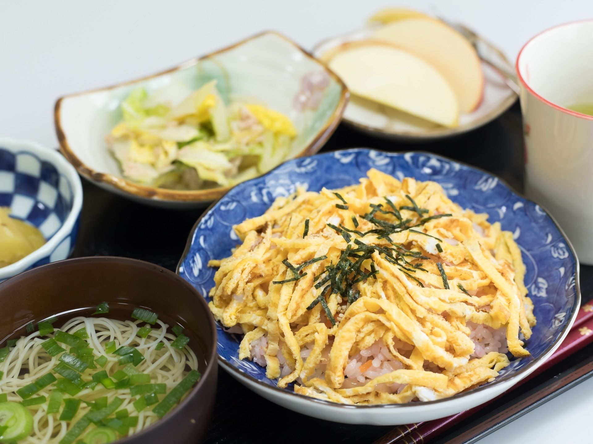 食事の一例の写真である。ちらしずしがメインの日は、汁物のにゅうめんが付き、デザートにリンゴが並んでいる。