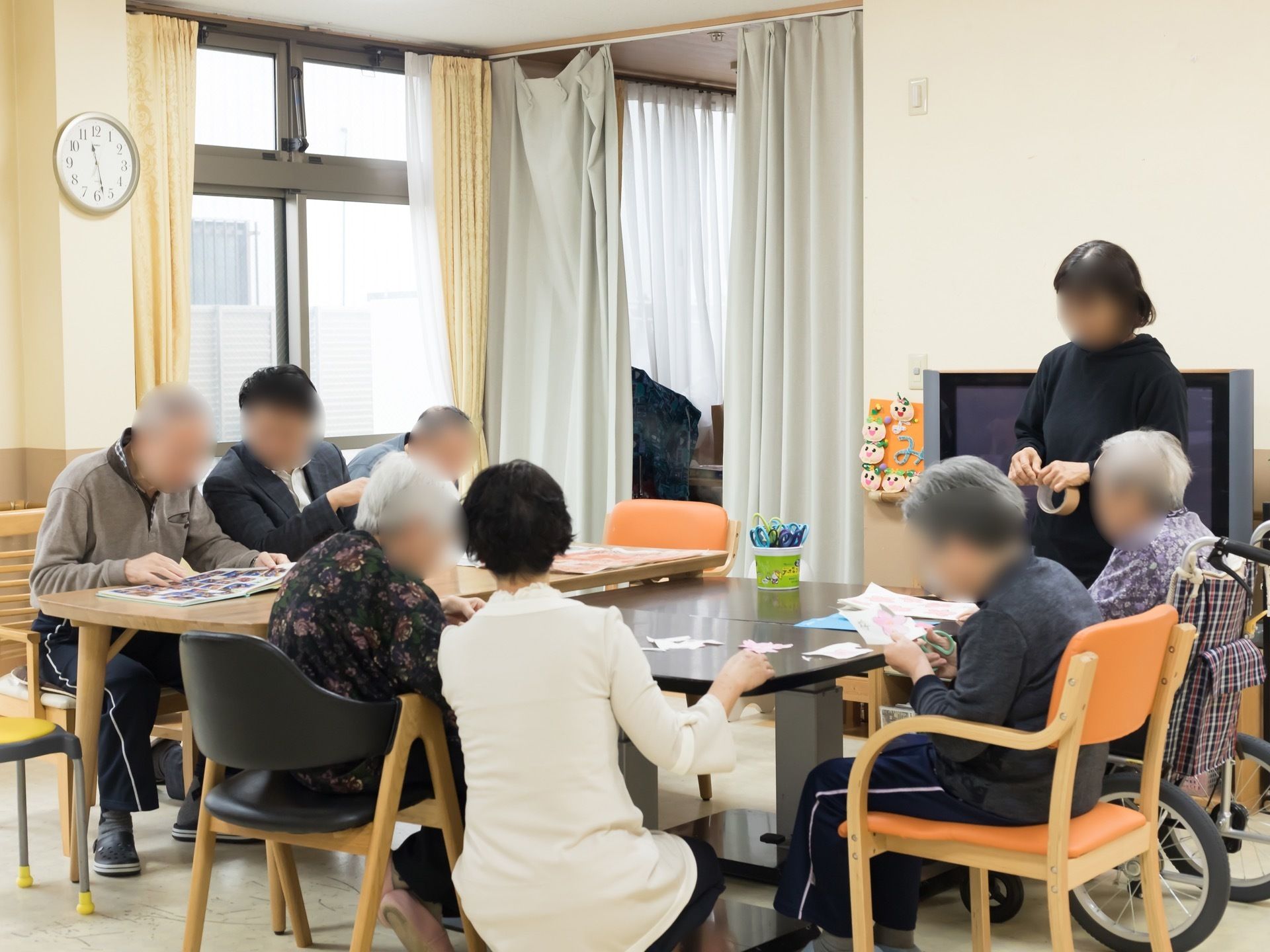 中央にテーブルセットが置かれた共有スペースで、たくさんの入居者様がレクリエーションやアルバム鑑賞を楽しんでいる。
