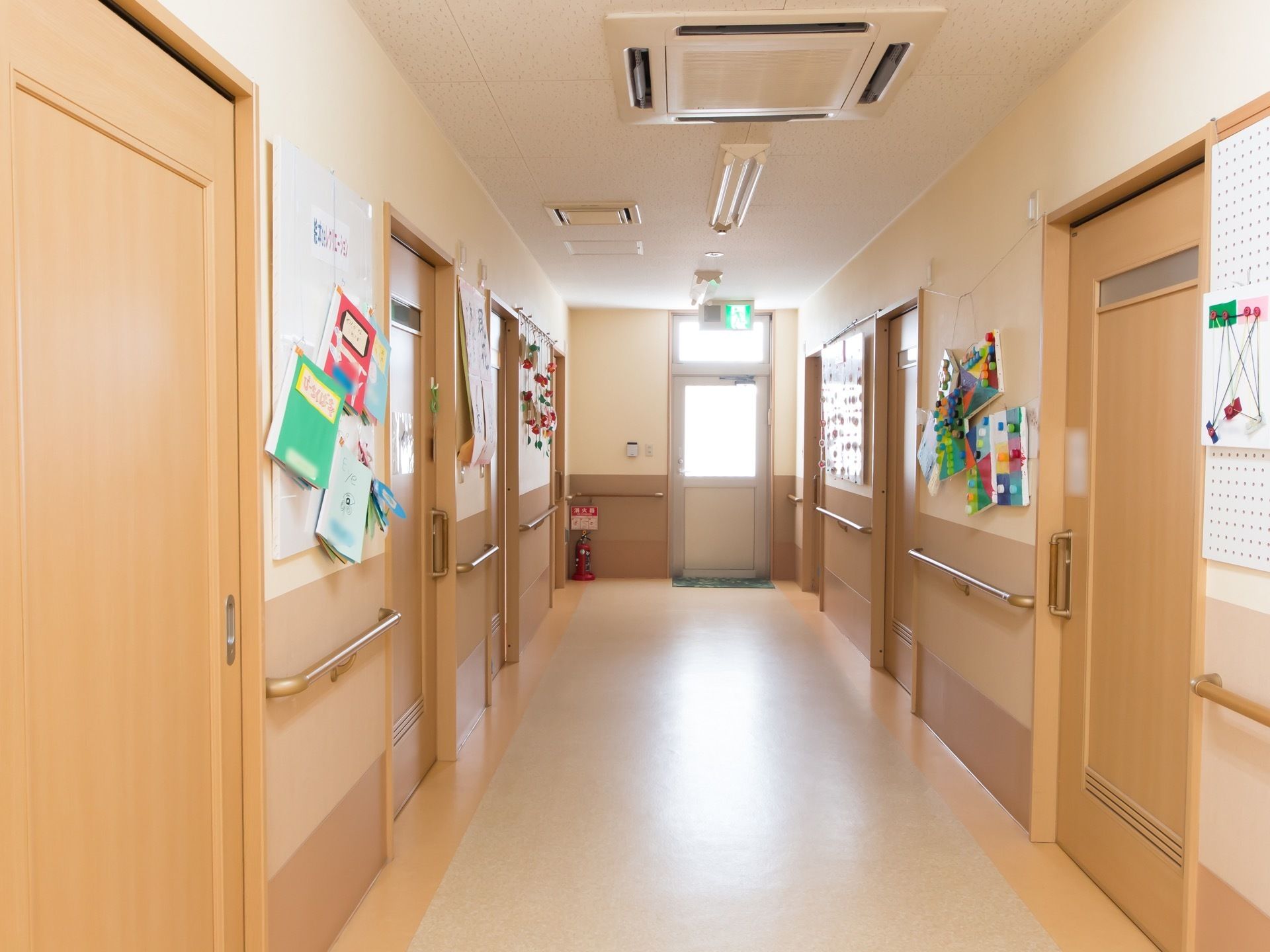 幅の広い廊下に居室へのドアが両側に並んでいる。突き当りは非常扉があり、床に消火器が置かれている。壁にノートなどが掛けられている。