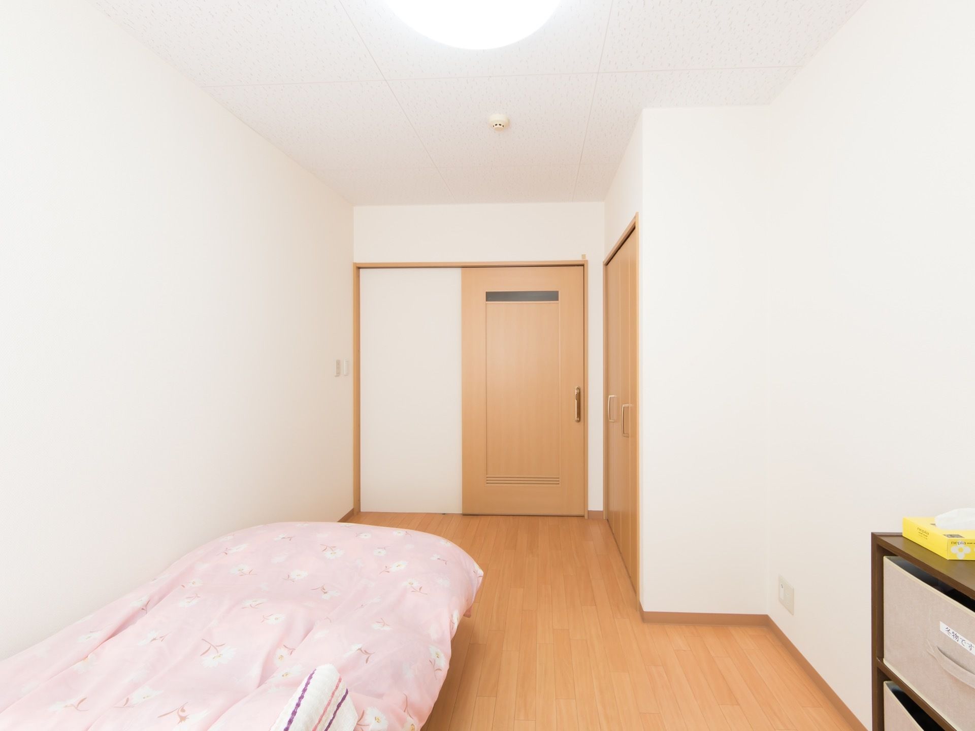 フローリングの居室で、壁際にピンクの布団が敷かれたベッドが置かれている。入口は木製の引き戸になっている。